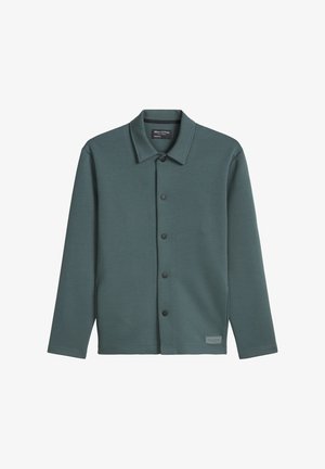 Dunkelgrüne langärmelige Jacke mit Knöpfen und Kragen, ausgestattet mit mattschwarzen Druckknöpfen und einem kleinen Stoffmarkenlabel nahe dem Saum.