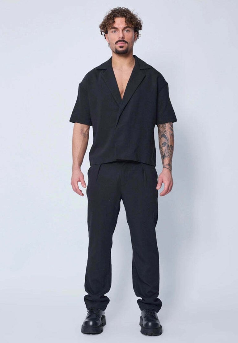 Chemise noire à manches courtes avec col associée à un pantalon noir à taille élastique. Les deux sont en tissu doux et léger. Bottes noires à lacets.