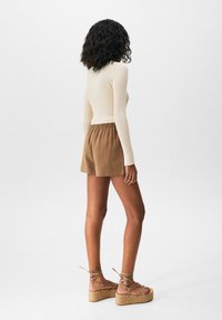 Haut crème à manches longues côtelé, short marron à taille élastique, et sandales compensées beige avec liens à la cheville. Accent sur les matériaux et les silhouettes ajustées.