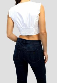 Top corto blanco con mangas con volantes y espalda fruncida, combinado con jeans ajustados de color azul oscuro que tienen bolsillos traseros y un acento de logotipo.