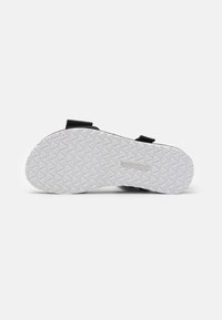 Sandal negra con suela blanca estampada, que cuenta con correas ajustables y plantilla texturada para un mejor agarre. Por debajo, diseño de banda de rodadura en forma de diamante.