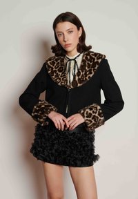 Black wool jacket with a leopard print fur collar and cuffs. Features a front zipper and a textured black ruffled skirt.