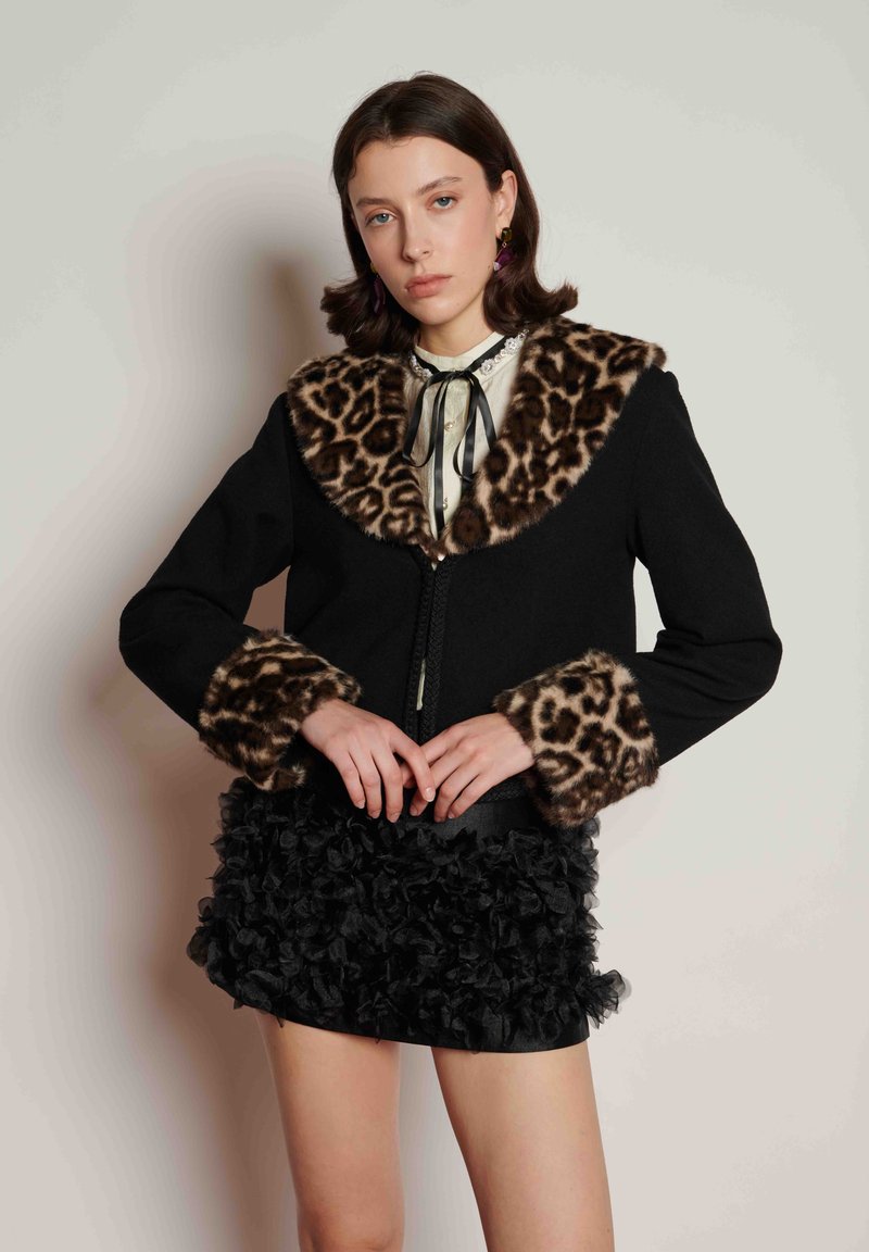 Black wool jacket with a leopard print fur collar and cuffs. Features a front zipper and a textured black ruffled skirt.