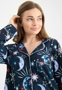 Navy pajama top with moon and star pattern in blue, white, and red. Features a notched collar and a chest pocket with white piping.