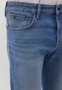 Light blue denim jeans featuring a classic five-pocket design, a small brand tag on the front pocket, and contrasting orange stitching.