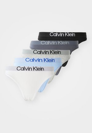 Penki Calvin Klein thong tipo apatiniai – balti, šviesiai mėlyni, pilki, tamsiai mėlyni ir juodi – išdėstyti krūvoje, matomi prekės ženklo logotipai.