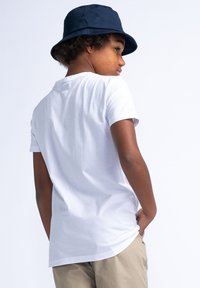 Camiseta blanca de manga corta con escote redondo, de tejido de algodón texturizado, combinada con pantalones cortos caqui y un sombrero de cubo azul marino.