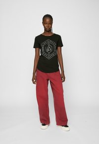 Svart bomullst-skjorte med et hvitt geometrisk "Linkin Park" grafisk design. Kombinert med løse røde jeans og svart-hvite sko.