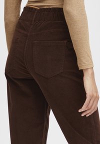 Brown corduroy trousers with an elastic waistband, featuring back pockets and a smooth texture. The fabric has a subtle ribbed pattern.