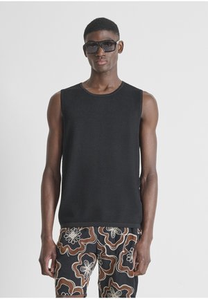 Joven con camiseta sin mangas negra y pantalones cortos negros con grandes patrones florales abstractos, mostrado sobre un fondo neutro.