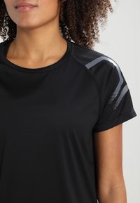 Camiseta deportiva negra de manga corta, con textura suave y detalles en gris metálico con patrones de puntos en el hombro.
