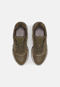 Olivegrüne Wildleder- und Mesh-Sneaker verfügen über eine Schnürung, einen gepolsterten Kragen und eine weiße Gummisohle mit braunen Akzenten. Das Logo auf der Zunge ist sichtbar.