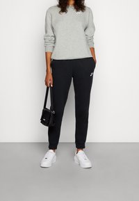 Felpa grigia, pantaloni sportivi neri, scarpe bianche. Caratterizzata da loghi Nike, una vestibilità comoda e una piccola borsa nera. Look semplice e sportivo.