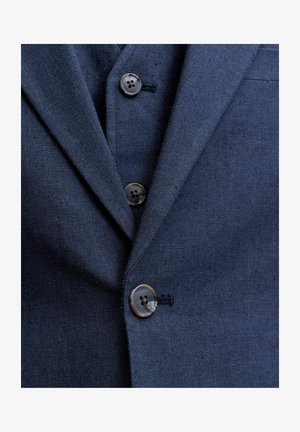 Lähikuva tummansinisen bleiserin edestä, jossa näkyy kolme ruskeaa nappia ja rintatasku teksturoidulla kankaalla.