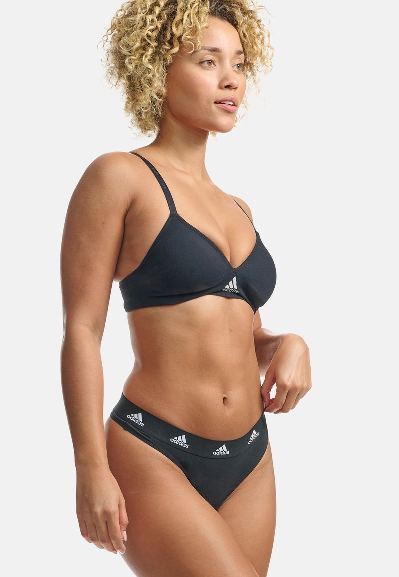 Černý bikiny set obsahující trojúhelníkový bralet s tenkými ramínky a odpovídající tanga, obě s bílými logovými akcenty a elastickými pásky.