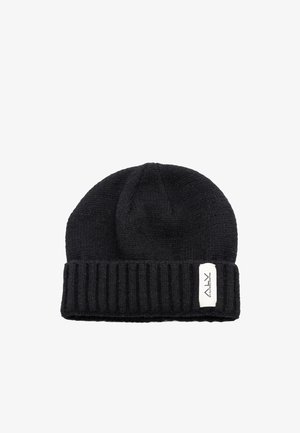 Cappello nero lavorato a maglia con risvolto a coste. Presenta una cima piatta e una piccola etichetta bianca con testo nero sul lato. Texture morbida e design aderente.