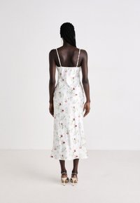 Maxi abito floreale in tessuto leggero, con spalline sottili regolabili, silhouette aderente e fondo bianco con motivi rosa e verdi.