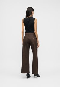 Καφέ παντελόνι με φαρδιά πόδια και ψηλή μέση, συνδυασμένο με εφαρμοστό μαύρο τοπ. Διαθέτει πίσω τσέπες και διακριτική λεπτομέρεια με λογότυπο της μάρκας.