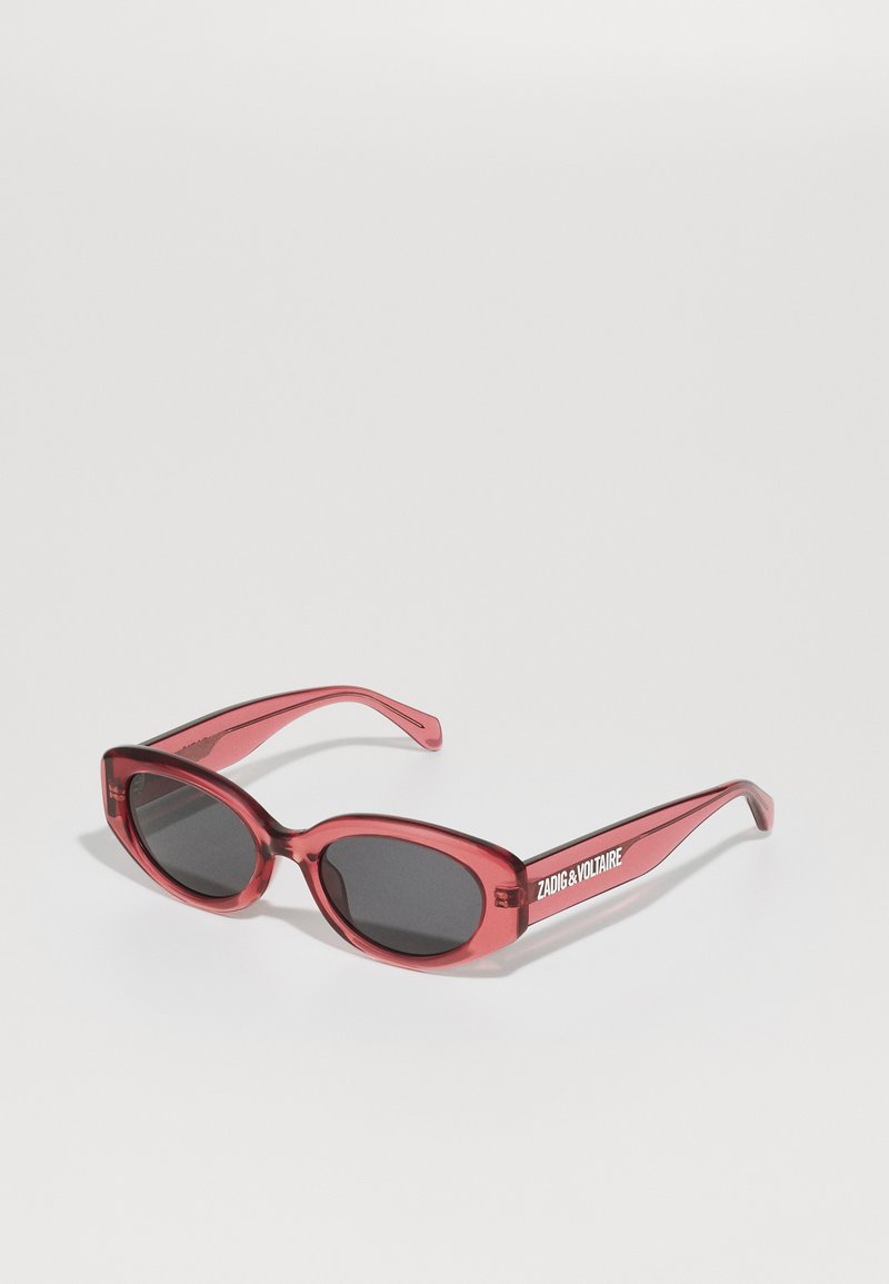 Czerwone przezroczyste okulary przeciwsłoneczne o zaokrąglonym prostokątnym kształcie, ciemne soczewki, cienkie ramiona i logo "ZADIG & VOLTAIRE" z boku.