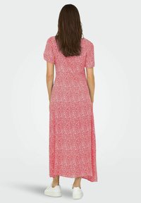 Abito maxi rosso con motivo floreale, maniche a sbuffo corte, vita aderente e gonna fluente. Indossato con sneakers bianche.