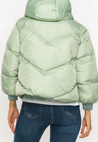 Kort pufferjakke i lys grøn, med høj krave, quiltet design og elastiske manchetter. Båret med mørkeblå jeans.