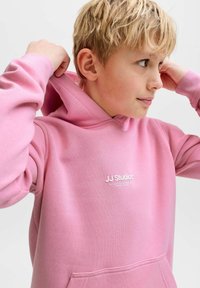 Lyserød hættetrøje lavet af blødt stof med en forlomme og snøre i hætten. Har "JJ Studios" logo broderet i hvidt på brystet.