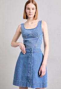 Farmer ruha, amelynek felül passzos, ujjatlan része van, alján pedig bővülő szoknyával. Világoskék színű, elöl gombos záródással és díszvarrással a mellen.