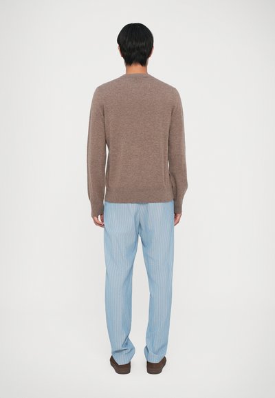 Pruun kootud kampsun ümmarguse kaelusega, koos helesiniste triibuliste püksidega ja pruunide kingadega, vaadatud tagant.