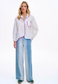 Biała koszula zapinana na guziki z różowymi i niebieskimi wykończeniami, w połączeniu z jasnoniebieskimi szerokimi dżinsami i zielonymi trampkami. Prosty design, luźny krój.