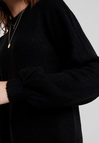 Pull noir avec une finition douce et texturée, épaules tombantes et poignets côtelés. Design simple, sans motifs ni pièces apparentes.