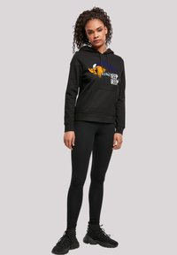 Sudadera negra con un gráfico de la cara de un personaje y el texto "BEEP BEEP" en blanco y azul. Combinada con leggings negros y calzado negro.