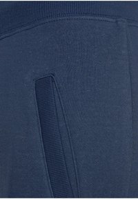 Nachtblaue Sweatpants mit glatter Textur, ausgestattet mit einer seitlichen Taschenöffnung und einem gerippten Bund für zusätzlichen Komfort.