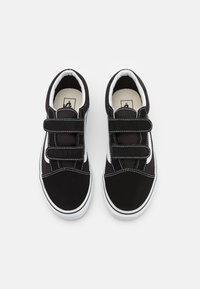 Black canvas shoes with white accents, two Velcro straps, rounded toe, stitched detailing, and a rubber sole.