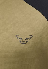 Λογότυπο με μαύρο στιλιζαρισμένο πρόσωπο πάνθηρα, στο κέντρο σε υφή ελιάς με μικρό τμήμα απλού μαύρου υφάσματος στην πάνω δεξιά γωνία.