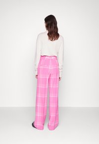 Pantalons large en tartan rose à taille haute ; avec des lignes à carreaux blanches. Le mannequin porte un haut à manches longues beige clair.