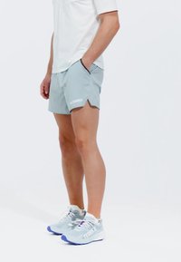 Pantalones cortos deportivos de color gris claro con bolsillos laterales, un dobladillo dividido y la palabra "TERREX" impresa en blanco. Combinados con zapatillas grises y blancas.
