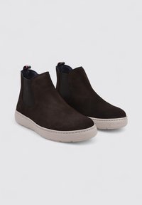 Bottines en suède marron foncé avec panneaux latéraux élastiques et une semelle en caoutchouc gris clair. Présente un tirant avec un accent rouge au talon.