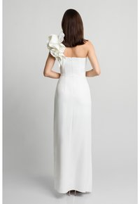 Biała sukienka bez ramiączek z dopasowaną górą i dużym falbanym akcentem na jednym ramieniu, charakteryzująca się gładkim, eleganckim materiałem i zapięciem na zamek.
