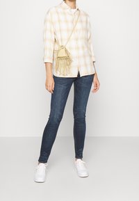 Rutig skjorta i kräm och ljusgul, parat med mörkblå skinny jeans och vita sneakers. Liten fransad axelväska i tan.