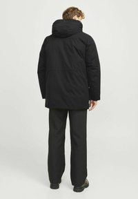 Chaqueta aislante negra con capucha, con corte recto, textura suave y costuras ocultas. Se lleva con pantalones y botas negras.