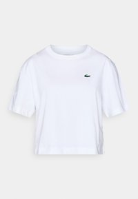 Λευκό crop t-shirt από βαμβάκι με κοντά μανίκια, με μικρό πράσινο λογότυπο Lacoste στο στήθος και διακριτικό μοτίβο σε όλο το ύφασμα.