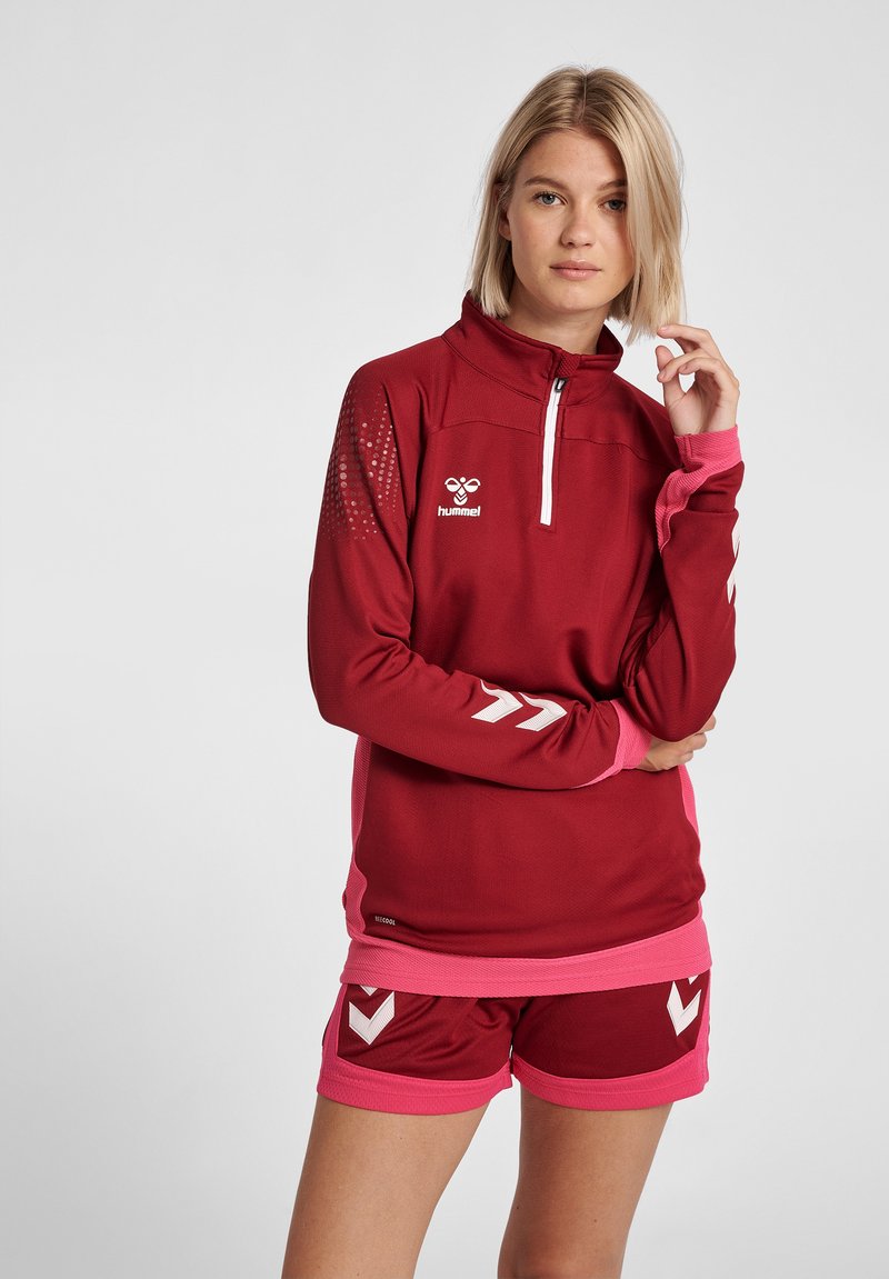 Bordeaux atletisk pullover med hvid lynlås og logo, har rosa accenter på ærmer og kant, parret med matchende bordeaux shorts med rosa detaljer.