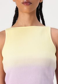 Close-up van een persoon die een mouwloos geribbeld topje draagt met een verloop van geel aan de bovenkant naar licht paars aan de onderkant.
