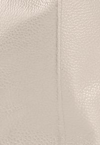 Cuir beige texturé avec une surface légèrement grainée. Le détail de la couture visible améliore le design, mettant en valeur la qualité du matériau.