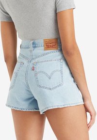 Light blue denim shorts with a high waist, frayed hem, and distinctive back pockets featuring a curved stitch pattern. Leather brand patch at back.