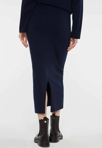 Marineblaue Strickrock mit einem Schlitz hinten, taillierte Form und gerippter Textur, kombiniert mit schwarzen Knöchelstiefeln mit goldenen Akzenten.