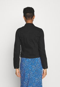 Czarna dżinsowa kurtka o dopasowanym kroju, z kołnierzykiem typu point i guzikami. Połączona z niebieską spódnicą w biało-czarny wzór.