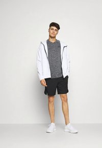 Sportinis komplektas, kuriame yra pilkas tekstūruotas marškinėlis, baltas su užtrauktuku striukė, juodi šortai ir balti sportbačiai. Aiškios linijos ir paprastas dizainas.