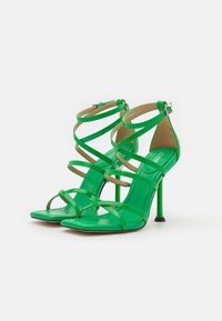 Sandali alti in pelle sintetica verde con cinturini incrociati multipli, punta quadrata e tacco a stiletto sottile.