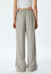 Pantalons gris clair, coupe décontractée, avec une taille froncée et des fentes sur les côtés. Fabriqués à partir d'un tissu texturé, présentant des rayures verticales noires sur les côtés.